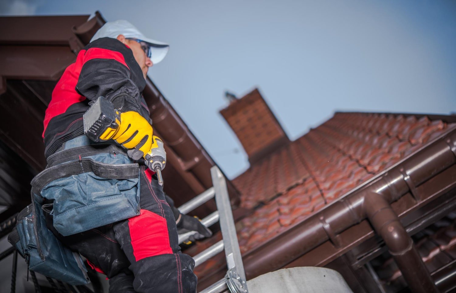 homme sur une échelle qui monte sur un toit avec une perceuse