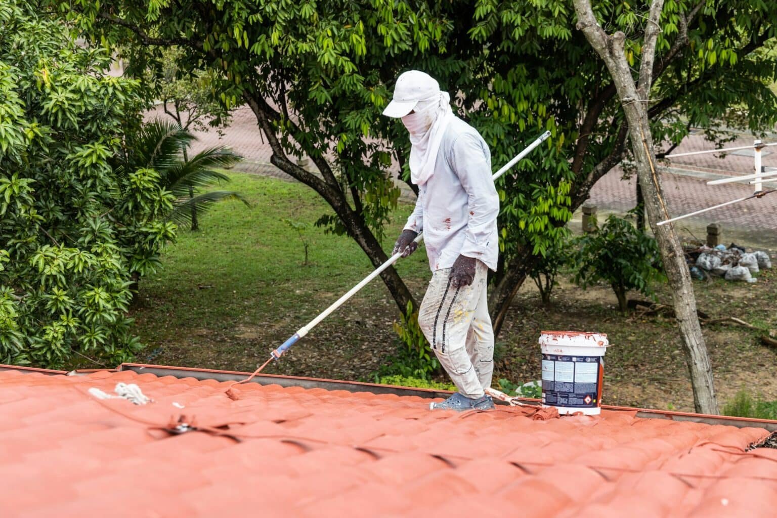 Homme en protection qui peint une toiture avec un rouleau